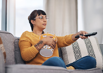 Buy stock photo Cropped shot of an attractive young woman sitting in her living room and watching a movie during a day off