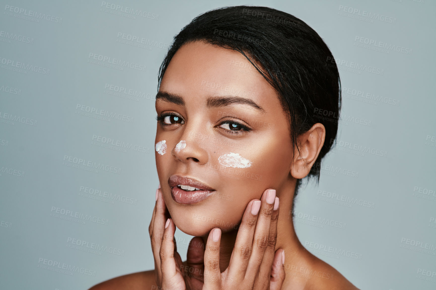 Buy stock photo Shot of a beautiful young woman applying moisturizer to her face