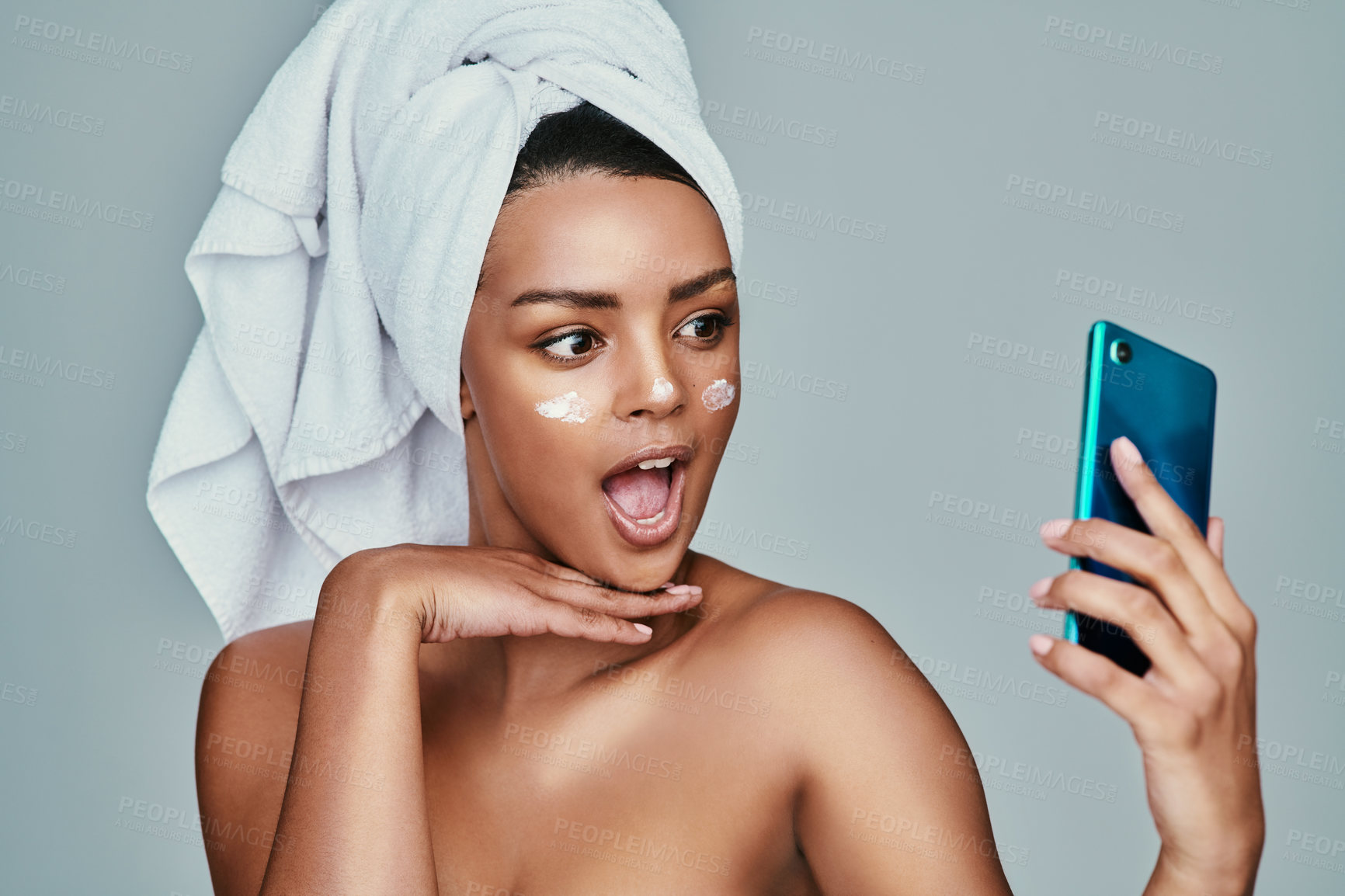 Buy stock photo Shot of a woman taking a selfie with a towel wrapped around her hair and moisturizer on her face