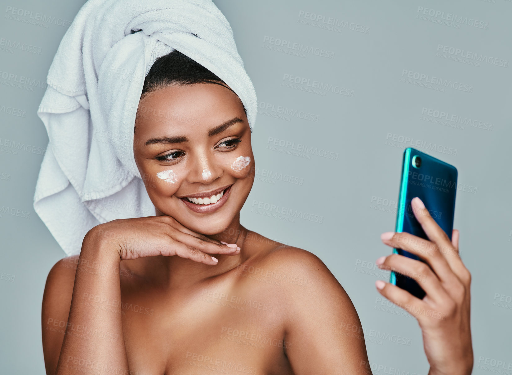 Buy stock photo Shot of a woman taking a selfie with a towel wrapped around her hair and moisturizer on her face