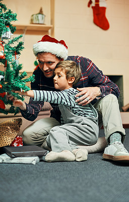 Buy stock photo Shot of an adorable little boy sitting next to the Christmas tree with his father