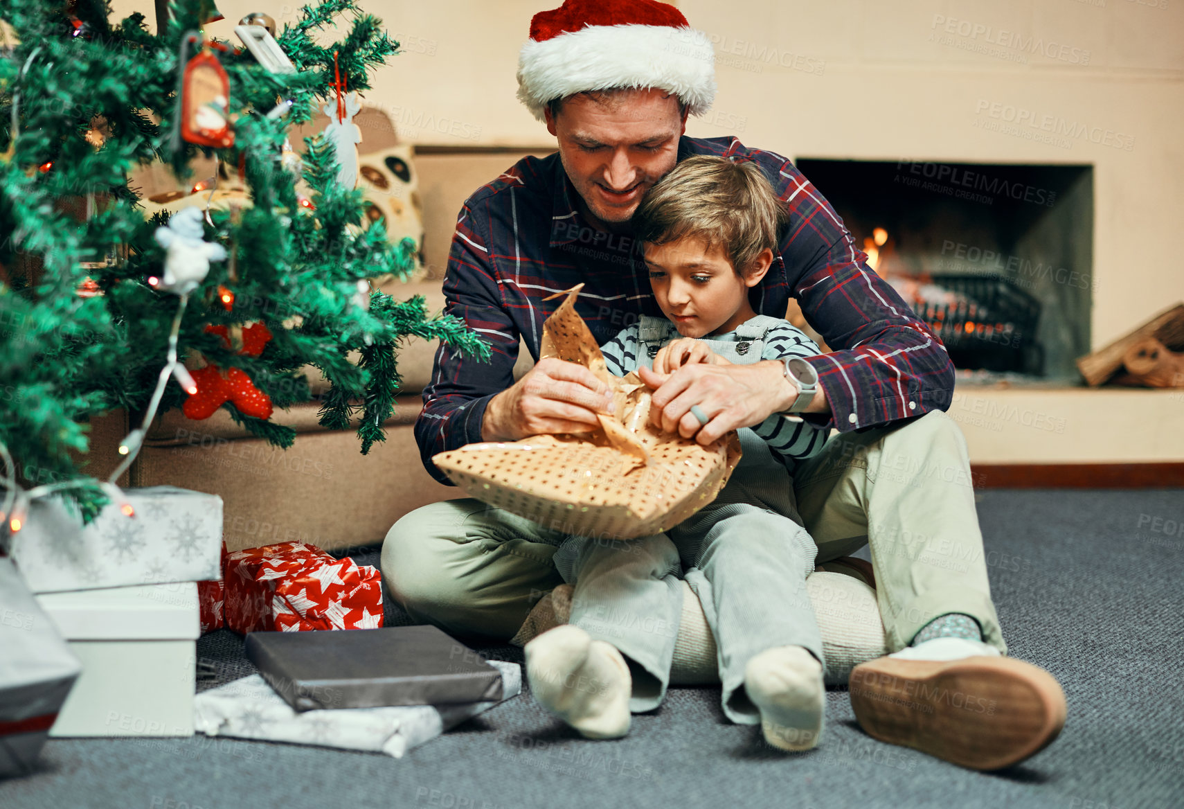 Buy stock photo Shot of an adorable little boy unwrapping Christmas presents with his father at home