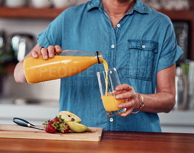 Buy stock photo Cropped shot of an unrecognizable senior woman pouring herself a glass of orange juice while preparing breakfast in the kitchen