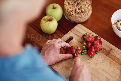 Buy stock photo High angle shot of an unrecognizable senior woman chopping up strawberries and other fruit while preparing breakfast in the kitchen
