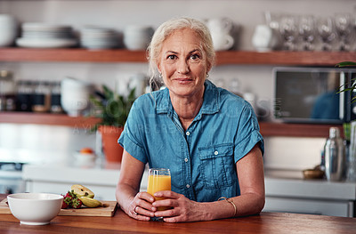 Buy stock photo Cropped portrait of an attractive senior woman enjoying a glass of orange juice while preparing breakfast in the kitchen