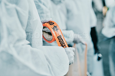 Buy stock photo Covid healthcare workers responding to a biohazard in a public area using barrier tape. First responders in protection hazmat suits cordoning a space due to a new pandemic or outbreak