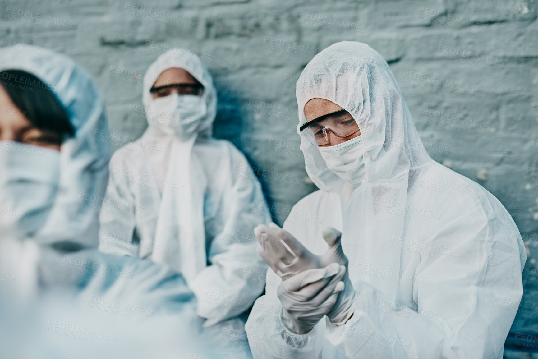 Buy stock photo Covid, pandemic and team healthcare workers wearing protective ppe to prevent virus spread at a quarantine site. Concerned first responder wearing a hazmat suit and checking his safety glove