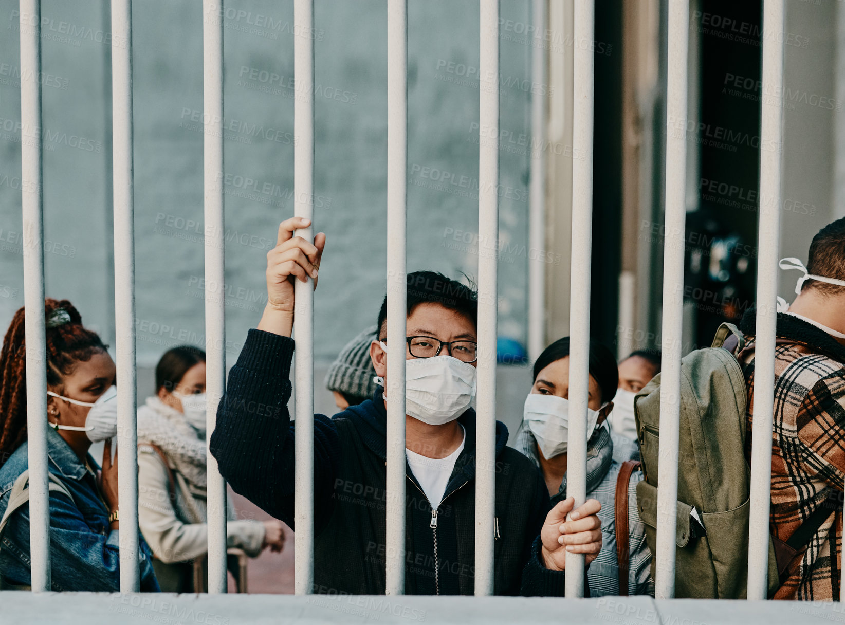 Buy stock photo Behind bars, lockdown and covid restrictions with a man wearing a mask during a pandemic and travel ban. Portrait of a male being locked out during the international or global corona virus outbreak