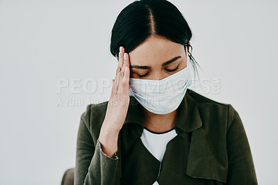 Buy stock photo Shot of a young woman experiencing a headache and wearing a mask against a studio background