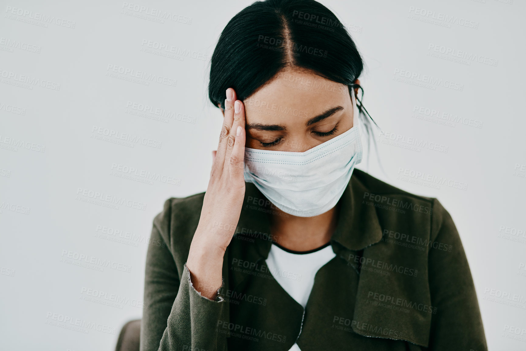 Buy stock photo Shot of a young woman experiencing a headache and wearing a mask against a studio background