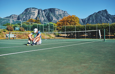 Buy stock photo Full length shot of a young male tennis player feeling tired and sitting down on a tennis court outdoors