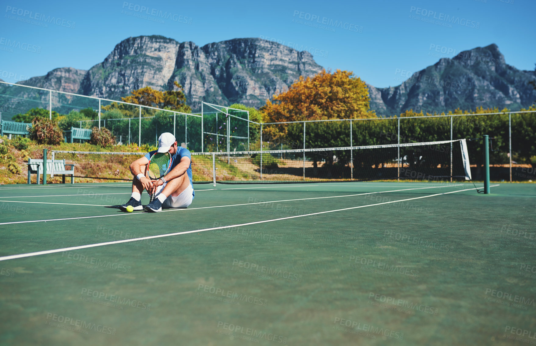 Buy stock photo Full length shot of a young male tennis player feeling tired and sitting down on a tennis court outdoors