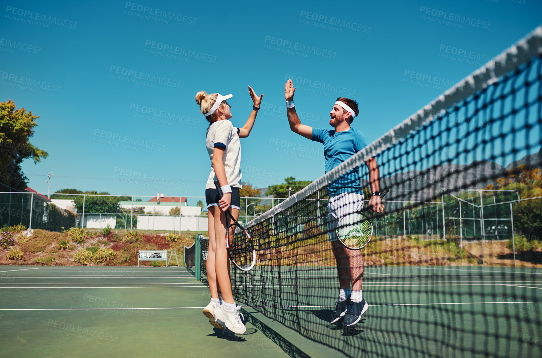 Buy stock photo Full length shot of two young tennis players giving each other a high five outdoors on the court