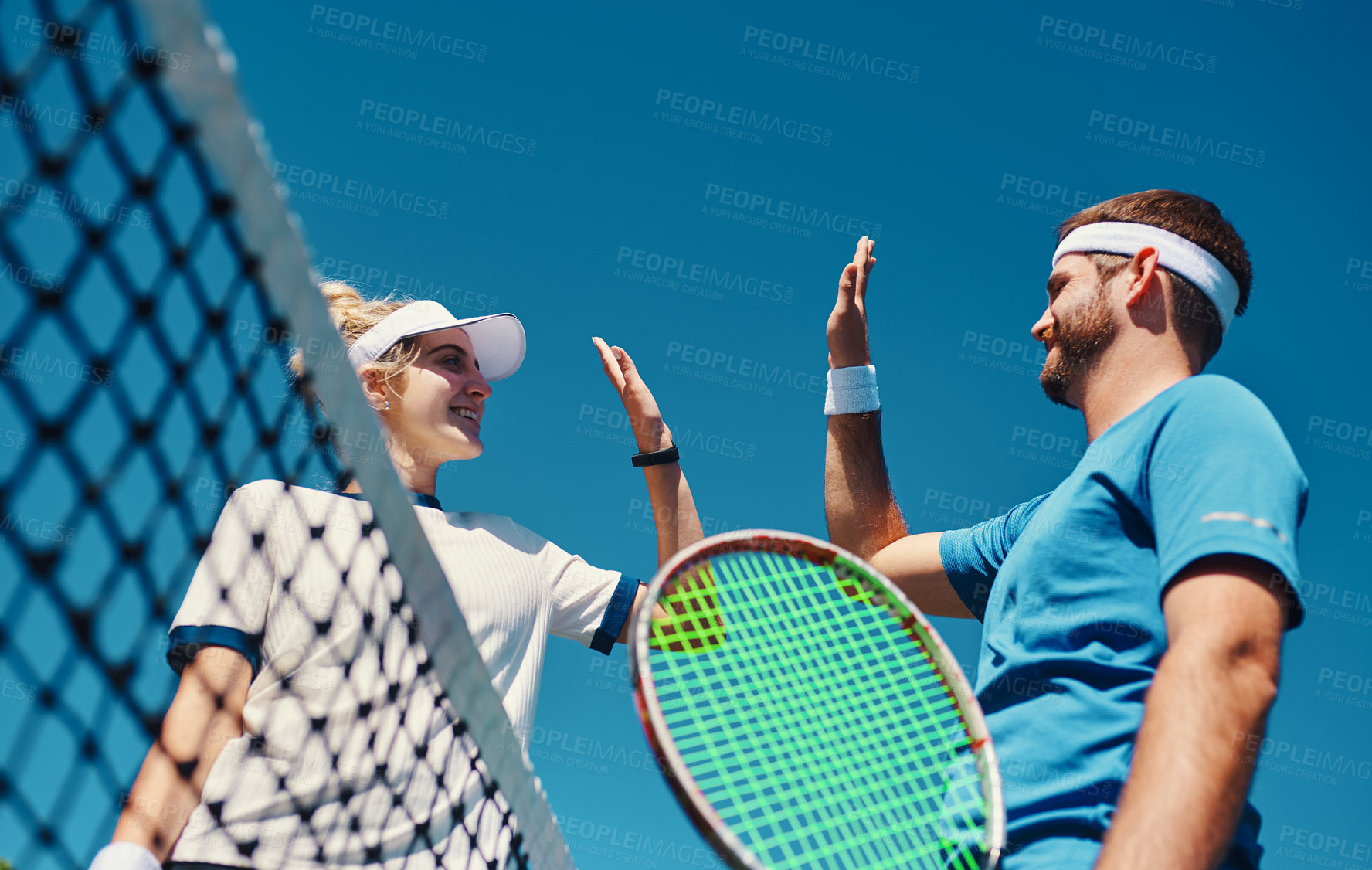 Buy stock photo Low angle shot of two young tennis players giving each other a high five outdoors on the court