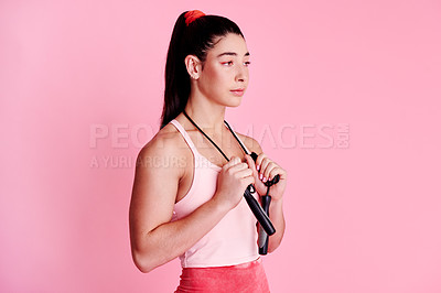 Buy stock photo Studio shot of a sporty young woman holding a skipping rope around her neck against a pink background