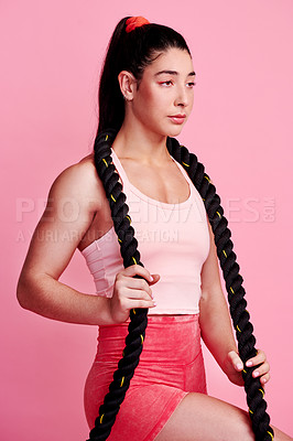 Buy stock photo Studio shot of a sporty young woman holding a battle rope around her neck against a pink background