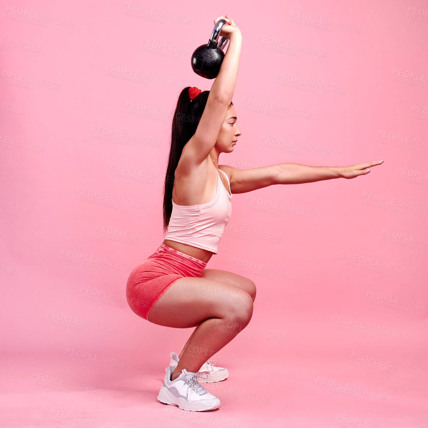 Buy stock photo Studio shot of a sporty young woman doing squats with a kettlebell against a pink background