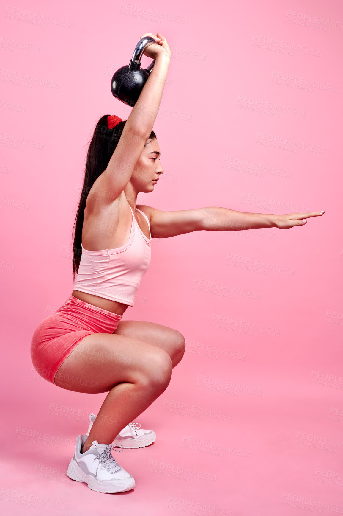Buy stock photo Studio shot of a sporty young woman doing squats with a kettlebell against a pink background
