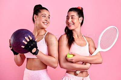 Buy stock photo Studio shot of two sporty young women holding sports equipment against a pink background