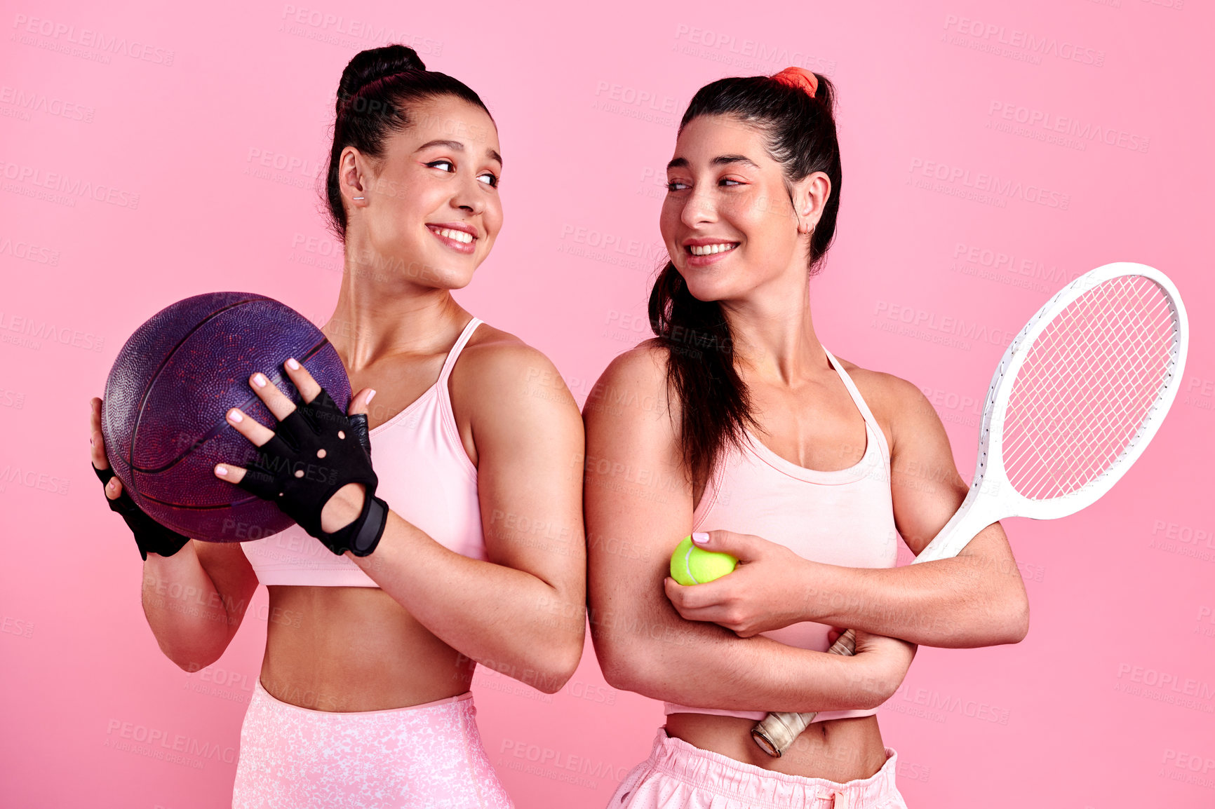 Buy stock photo Studio shot of two sporty young women holding sports equipment against a pink background