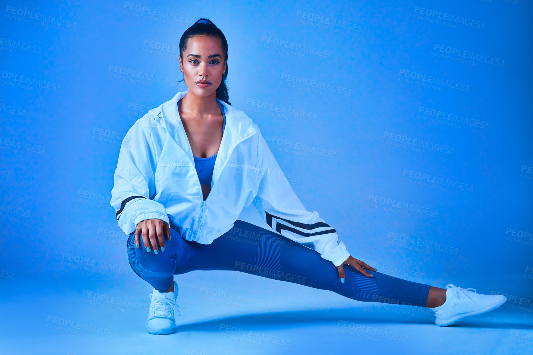 Buy stock photo Full length portrait of an attractive young female athlete stretching before a workout against a blue background