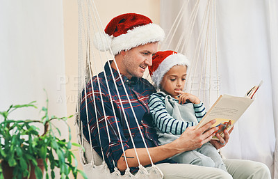 Buy stock photo Shot of a young man reading a book with his adorable son at Christmas