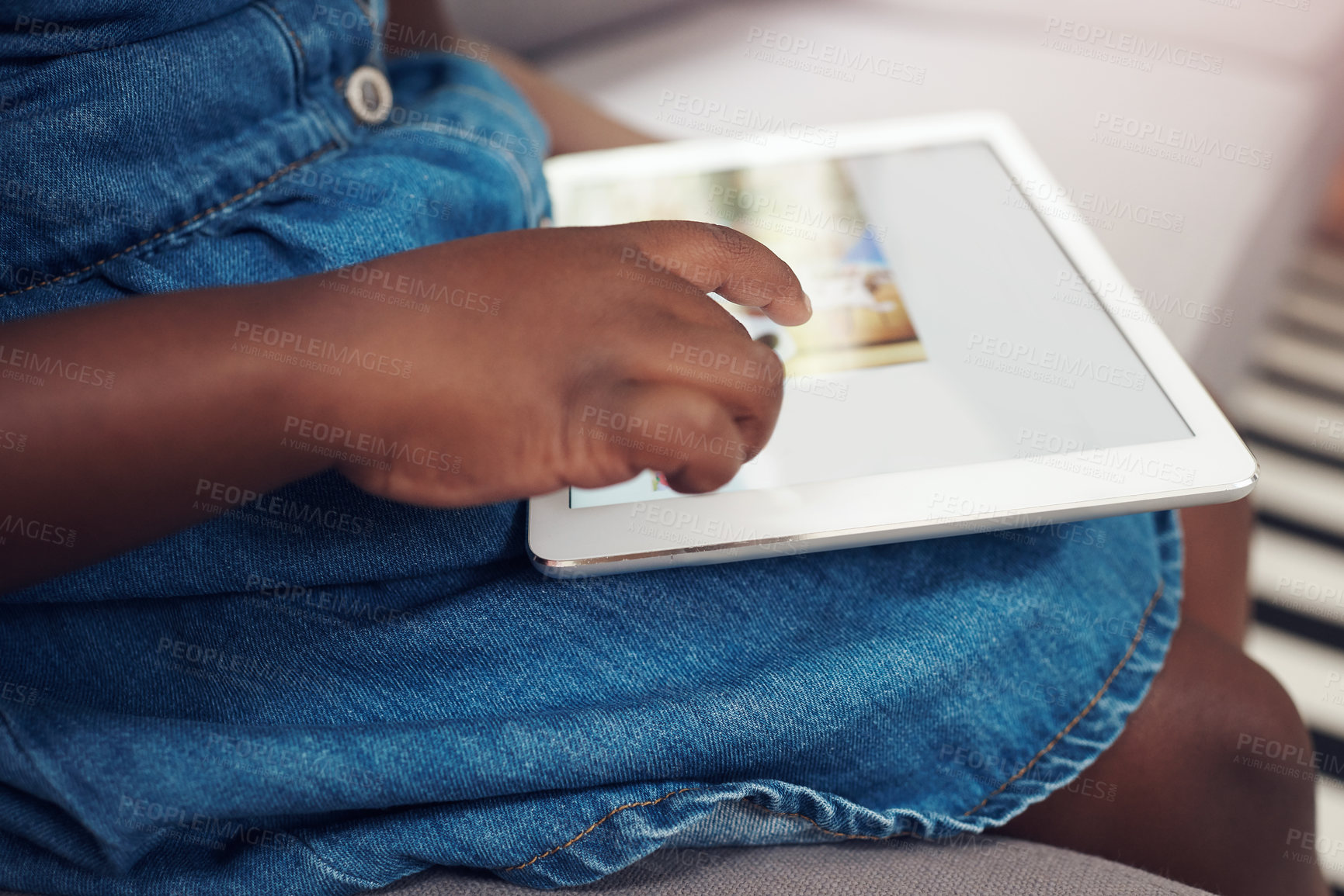 Buy stock photo Cropped shot of an unrecognizable little girl using a digital tablet while sitting on a sofa at home