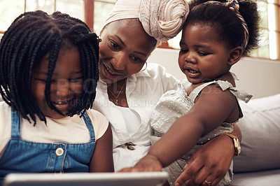Buy stock photo Cropped shot of two adorable little girls using a digital tablet while bonding with their mother at home