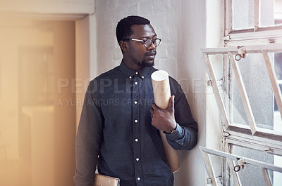 Buy stock photo Cropped shot of a handsome young male architect holding a scroll of blueprints while standing in a modern office