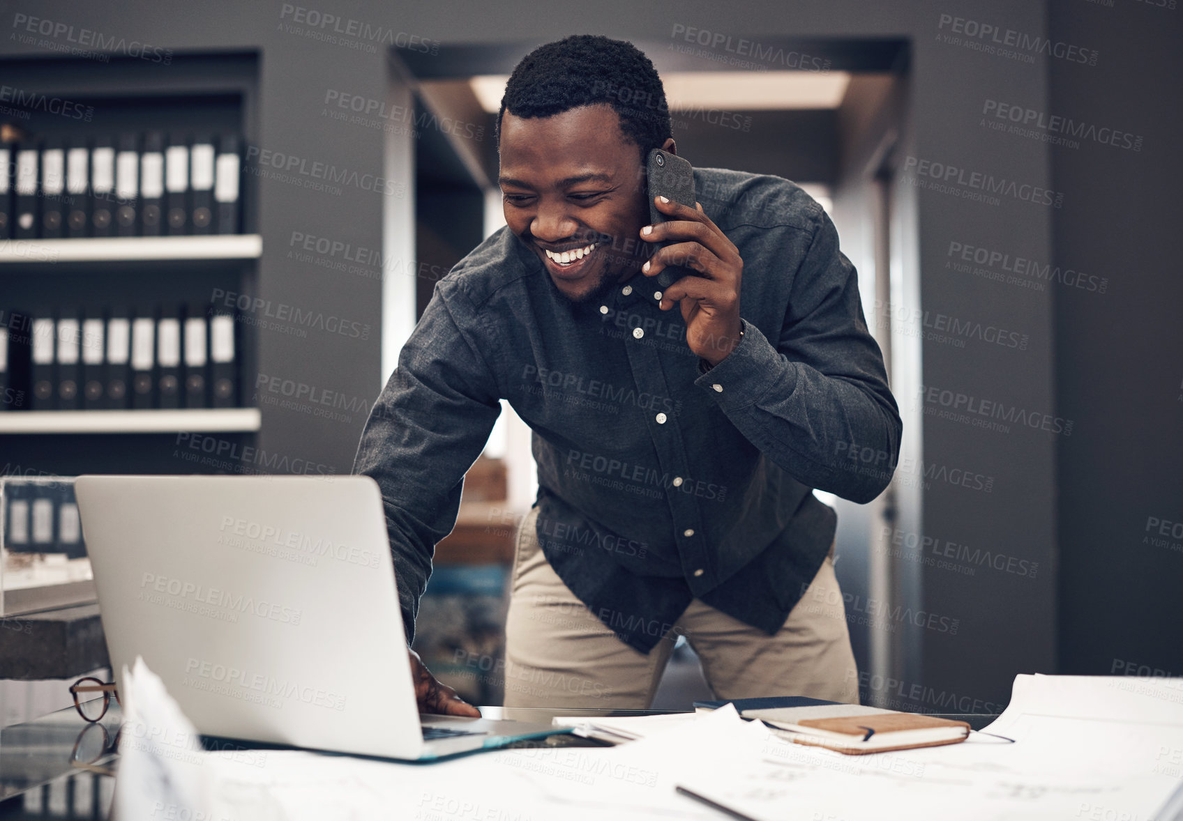 Buy stock photo Cropped shot of a handsome young male architect taking a phonecall while working on a laptop in a modern office