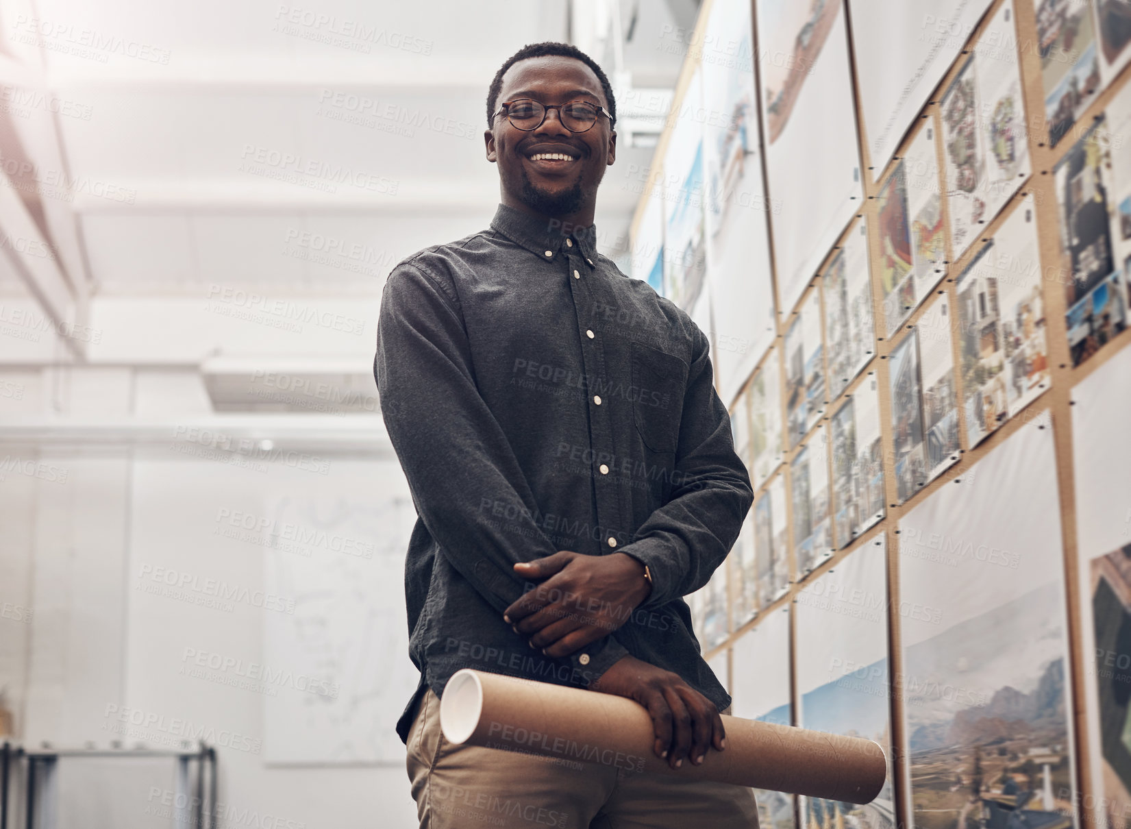 Buy stock photo Cropped portrait of a handsome young male architect smiling while holding a scroll of blueprints in a modern office
