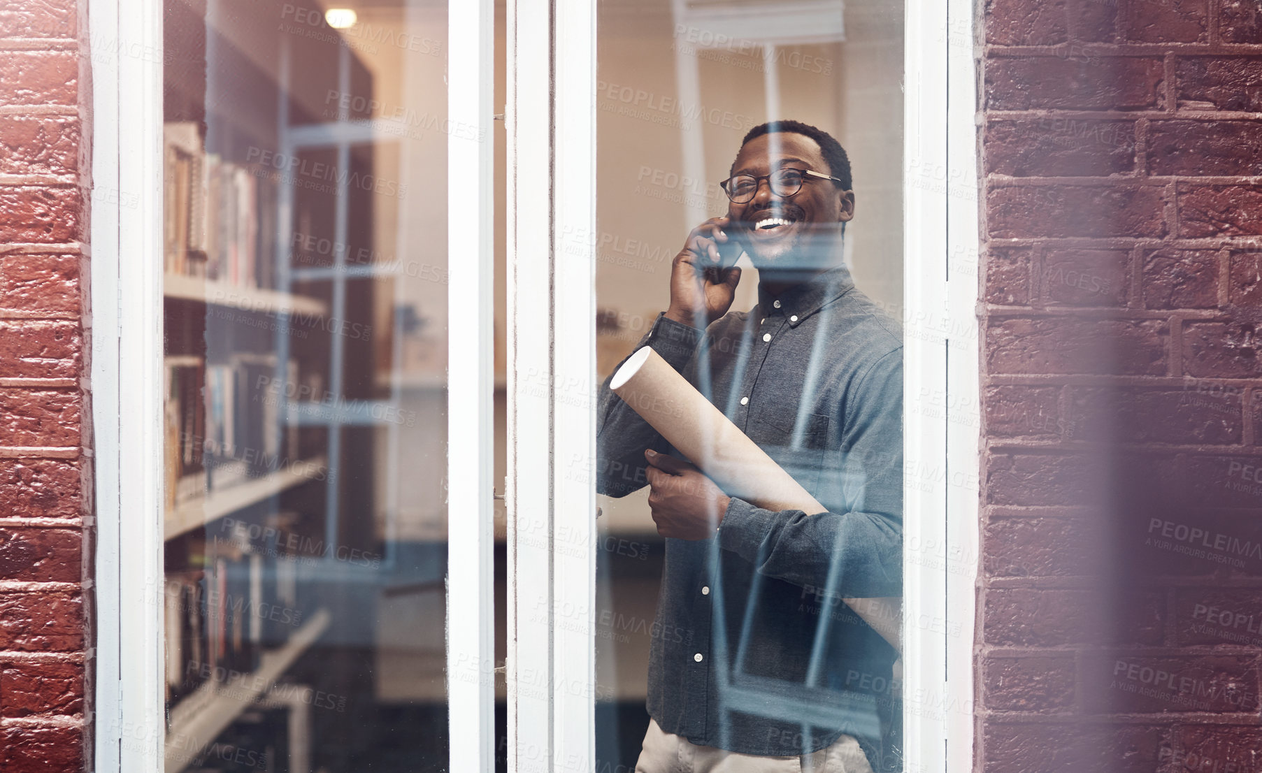 Buy stock photo Black man, architect and phone call in office, happy and paper roll for blueprint in negotiation with contractor. Person, smartphone and document by window in conversation, floor plan and decision