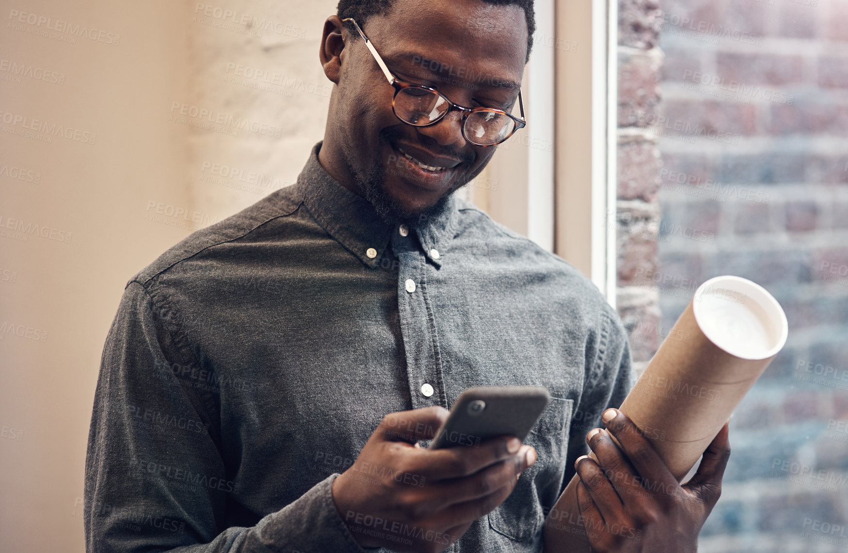 Buy stock photo Cropped shot of a handsome young male architect using a smartphone while standing in a modern office