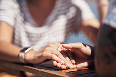 Buy stock photo Cropped shot of an unrecognisable couple holding hand while being on a lunch date outside next to a beach promenade