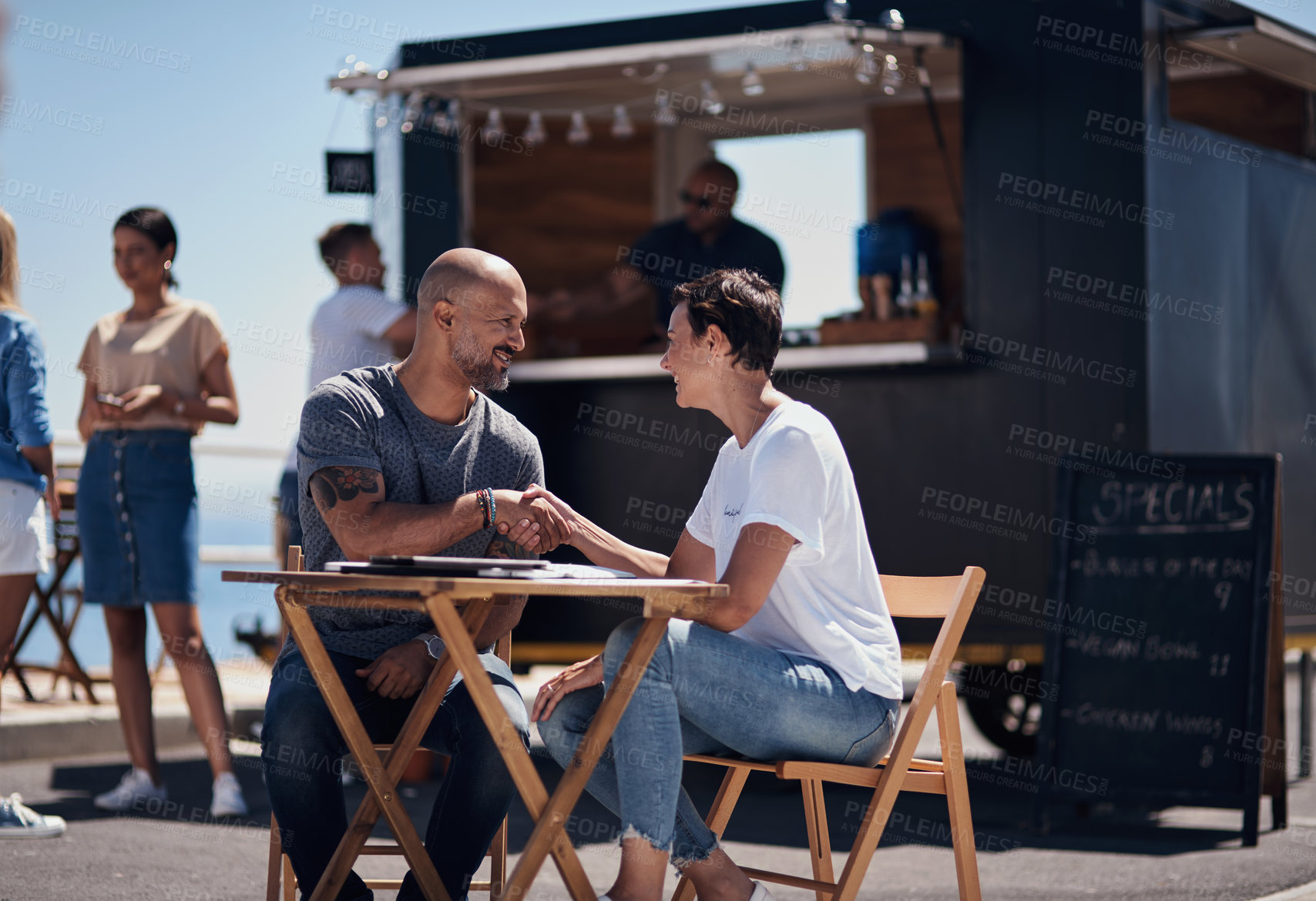 Buy stock photo Man, woman and handshake with happy conversation at harbor, bistro and meeting by restaurant in summer. Partners, talk and discussion with planning, business proposal or deal with promenade lunch