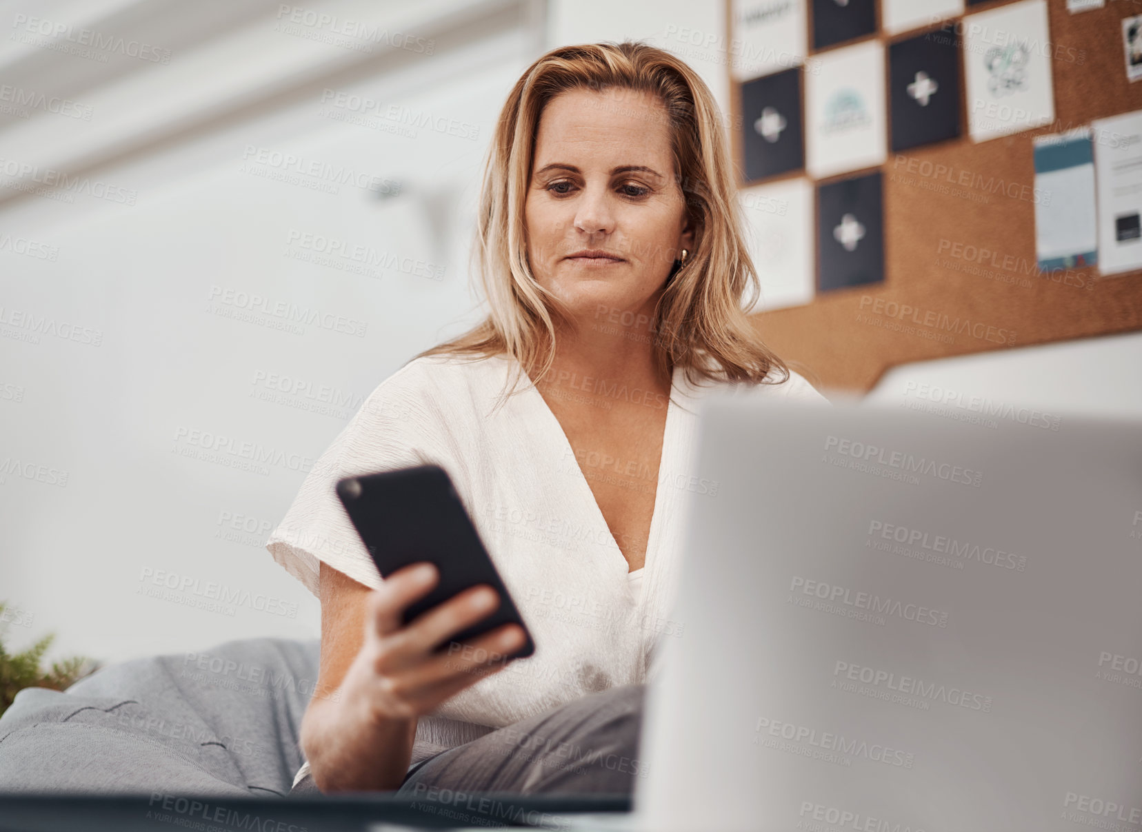 Buy stock photo Smartphone, business woman and reading email, social media or notification on laptop in startup. Mobile, typing and professional scroll online for article, blog or creative copywriter research info
