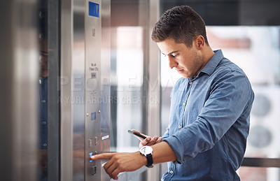 Buy stock photo Shot of a young businessman using a cellphone while pushing a button in an elevator
