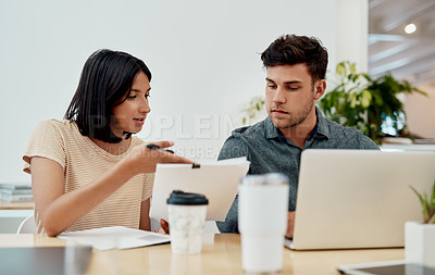 Buy stock photo Cropped shot of two young businesspeople sitting together in the office and going through paperwork