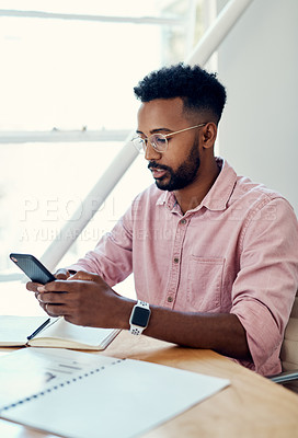 Buy stock photo Cropped shot of a handsome young businessman sitting alone and using his cellphone in the office