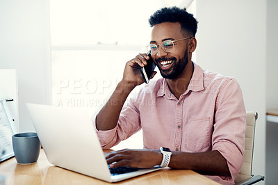 Buy stock photo Cropped shot of a handsome young businessman sitting and using his cellphone while working on his laptop in the office