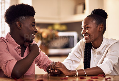 Buy stock photo Cropped shot of an affectionate young couple holding hands while sitting together in their kitchen on Valentine's day