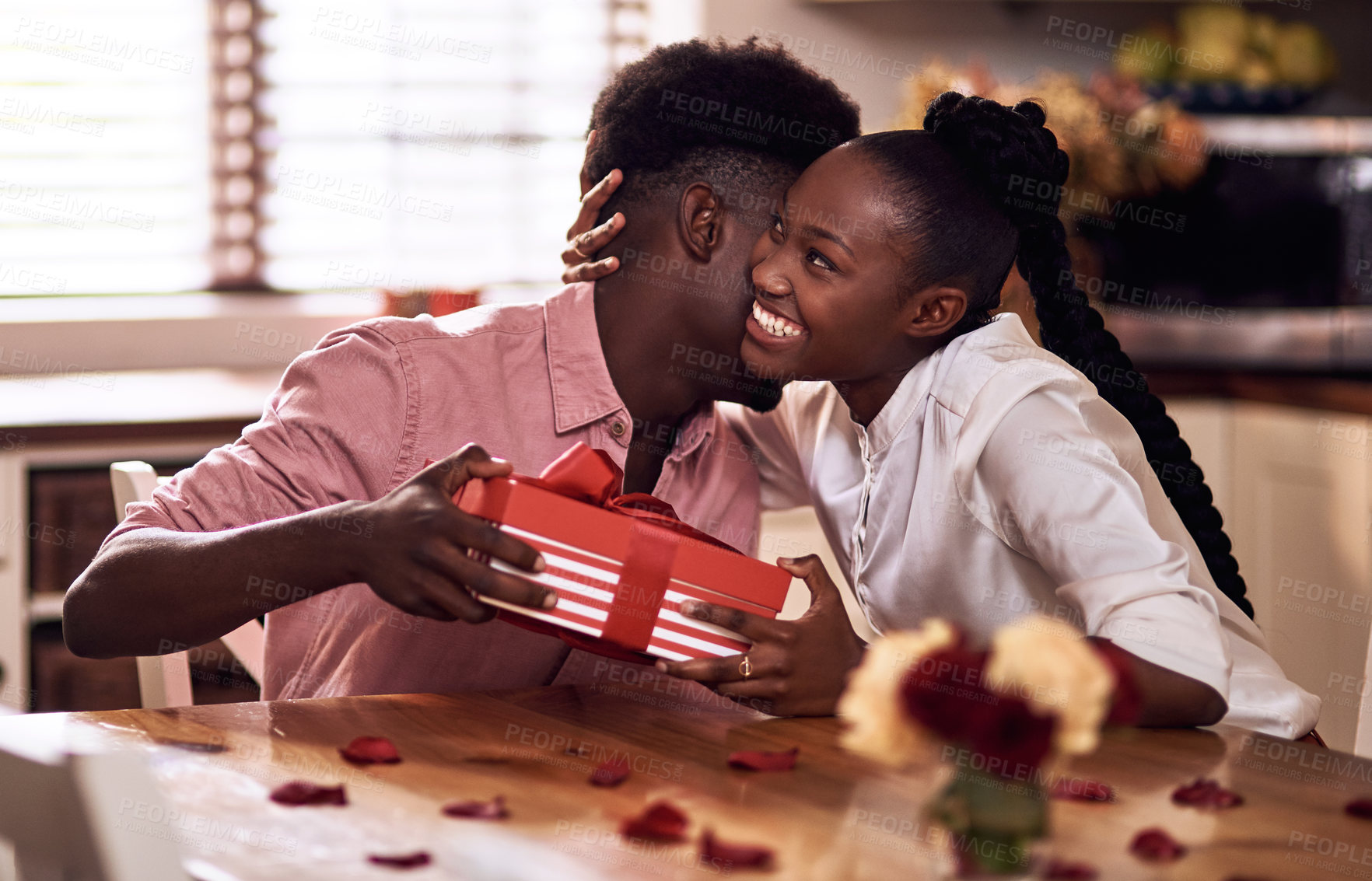 Buy stock photo Black couple, love and hug for gift in home with valentines day, happy bonding and healthy marriage. African man, woman and giving present with embrace for anniversary celebration, loyalty and smile