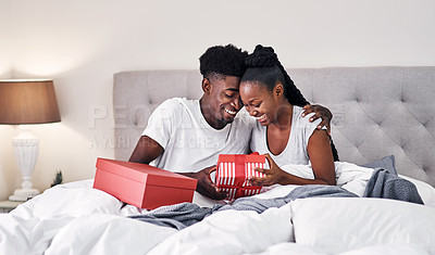 Buy stock photo Shot of a young couple exchanging gifts while sitting on their bed