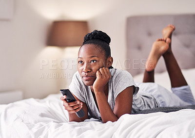 Buy stock photo Shot of a young woman holding a remote control while lying on her bed