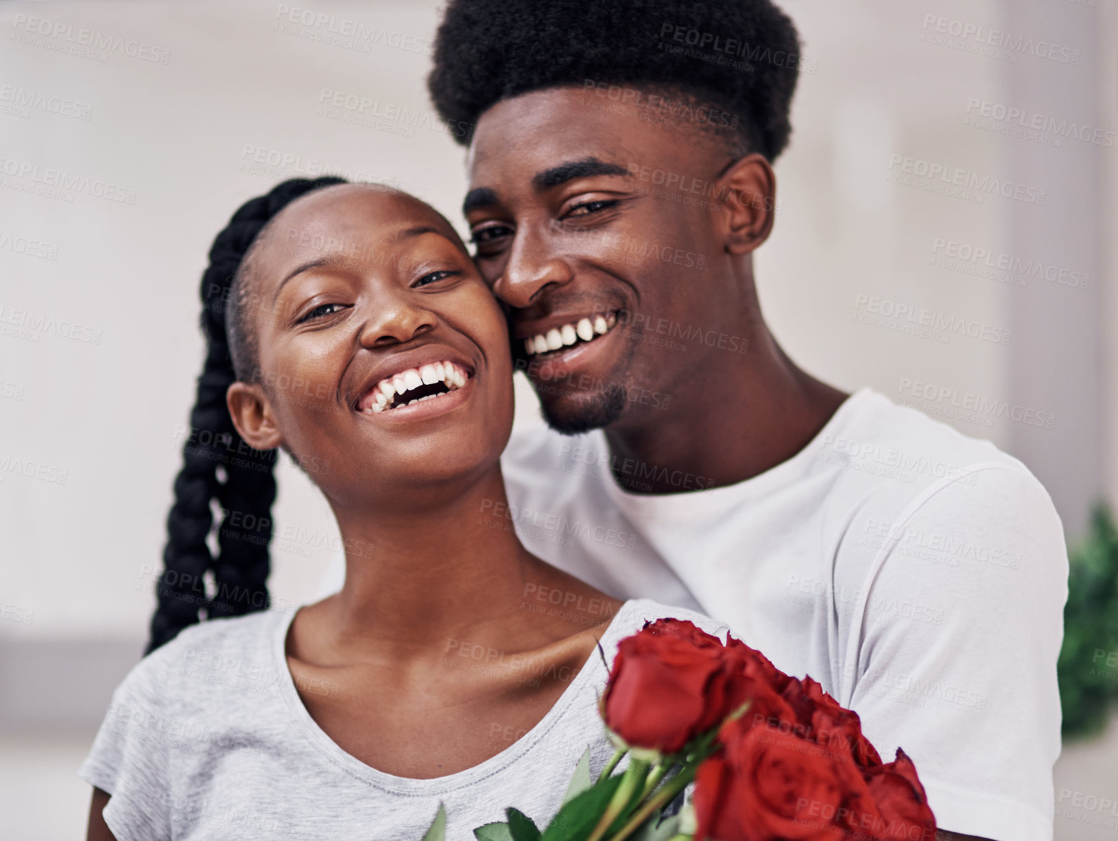 Buy stock photo Shot of a young woman holding a bunch of red roses while standing with her boyfriend at home