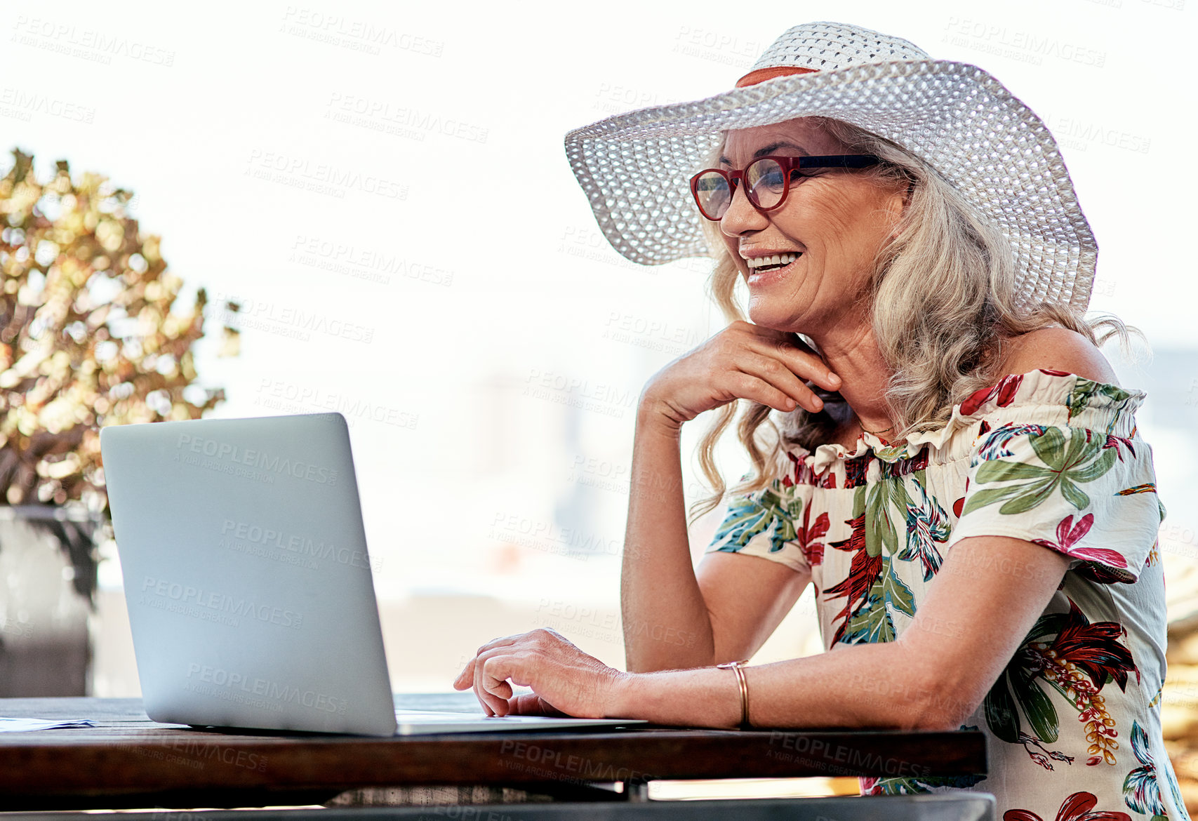 Buy stock photo Laptop, outdoor and happy senior woman laugh at funny joke, meme or reading email. Computer, retirement and person in summer hat to watch comedy video, news and relax on holiday or vacation at table