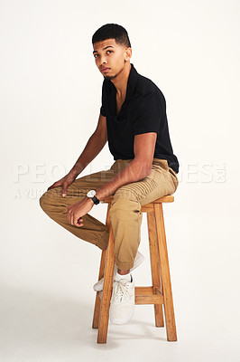 Buy stock photo Portrait of a handsome young man striking a pose while being seated on a chair against a grey background inside of a studio