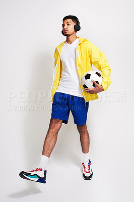 Buy stock photo Studio shot of a handsome young man listening to music while holding a soccer ball inside of a studio