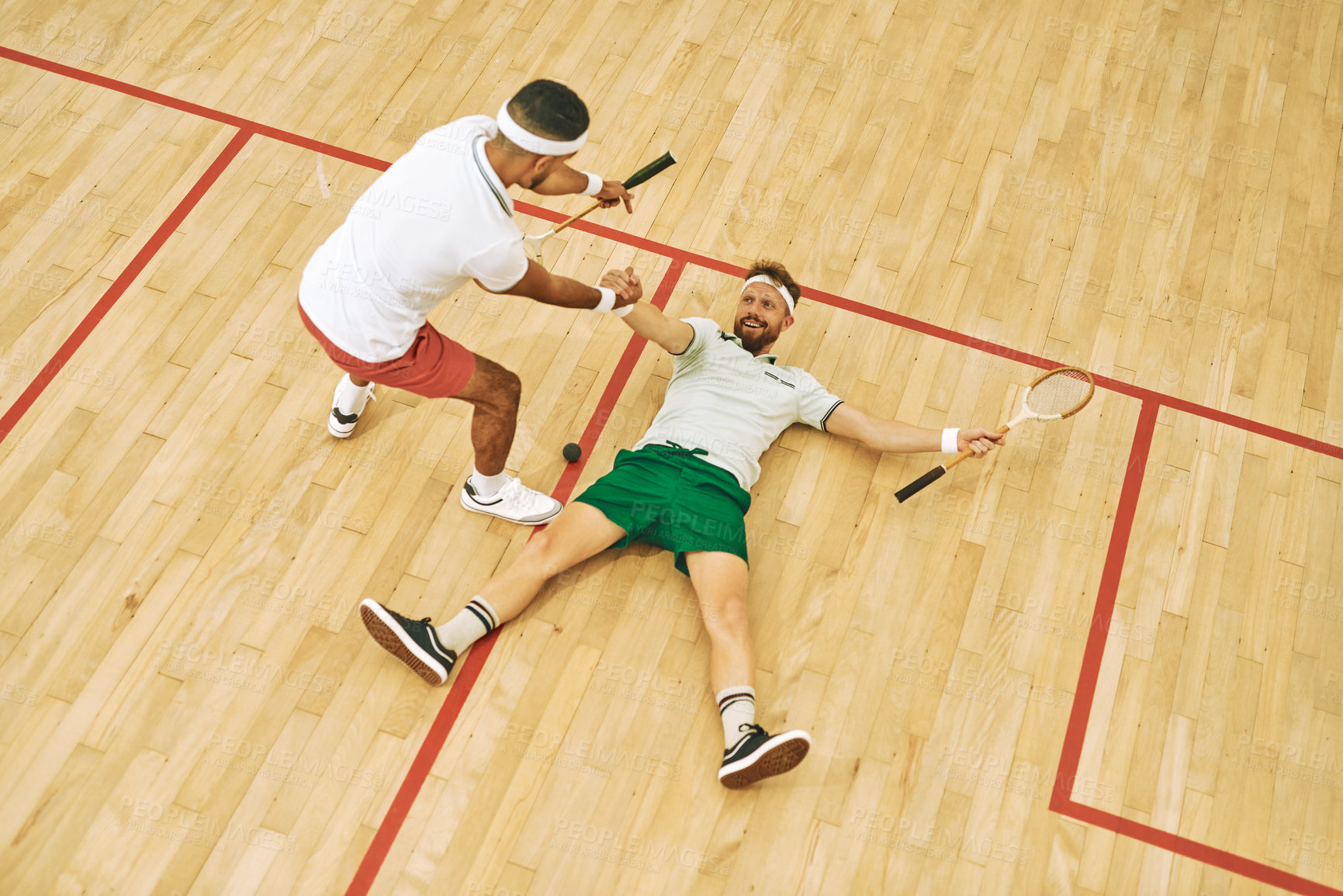 Buy stock photo High angle shot of a young man helping his friend up while playing a fame of squash