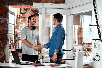 Buy stock photo Cropped shot of two young businessmen shaking hands in an office inside their workshop